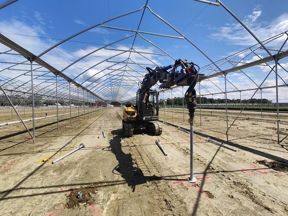Excavator installing screw piles under polytunnel frame